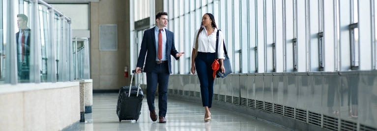 A man and a woman walk carrying luggage walk through an airport