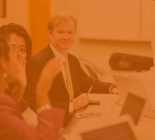 Business professionals sit at a conference table.