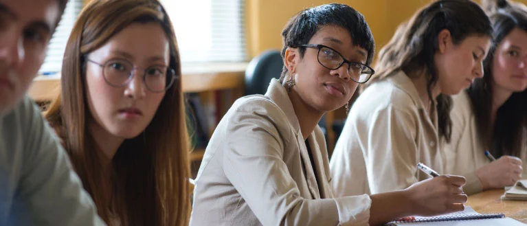 A group of business students sit at a table and take notes