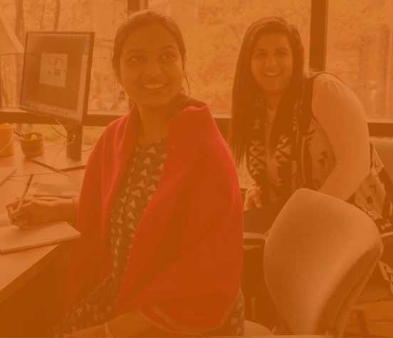 Two women sit at a desk in front of a window