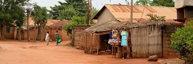 A small village with two people walking down a dirt road